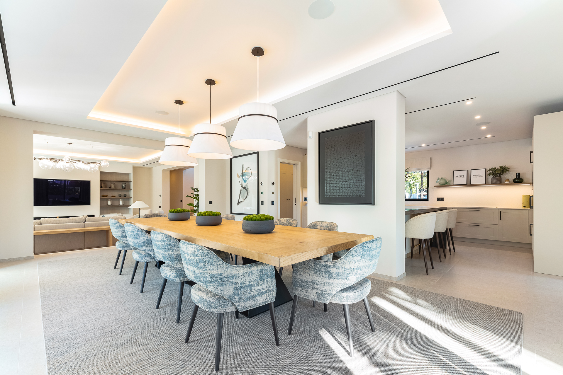 Contemporary open plan dining area with a solid timber table, upholstered chairs and pendant lighting beside a modern kitchen